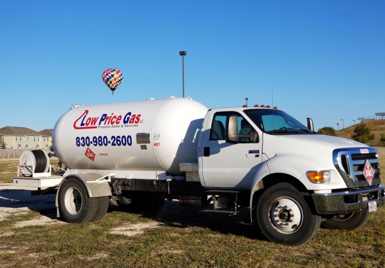 White gas delivery truck with logo and phone number parked on grassy lot under blue sky