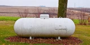 White propane tank in a grassy field beside a tree and farmland