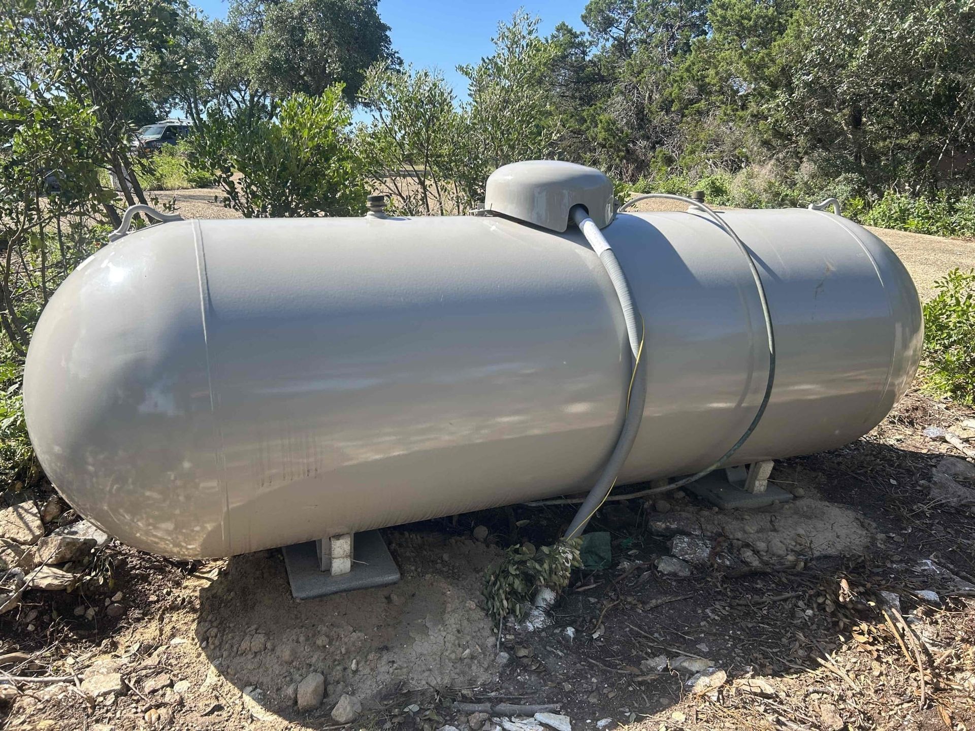Large silver propane tank outdoors on a gravel pad with trees in the background