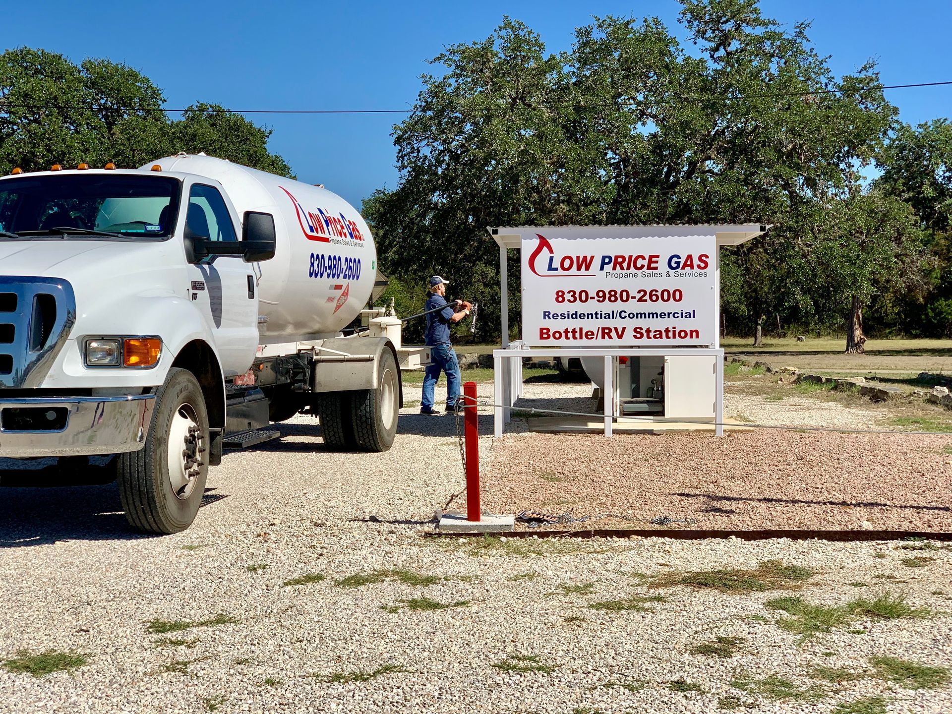 White water truck beside a “Low Price Gas” sign on a gravel roadside lot under a blue sky