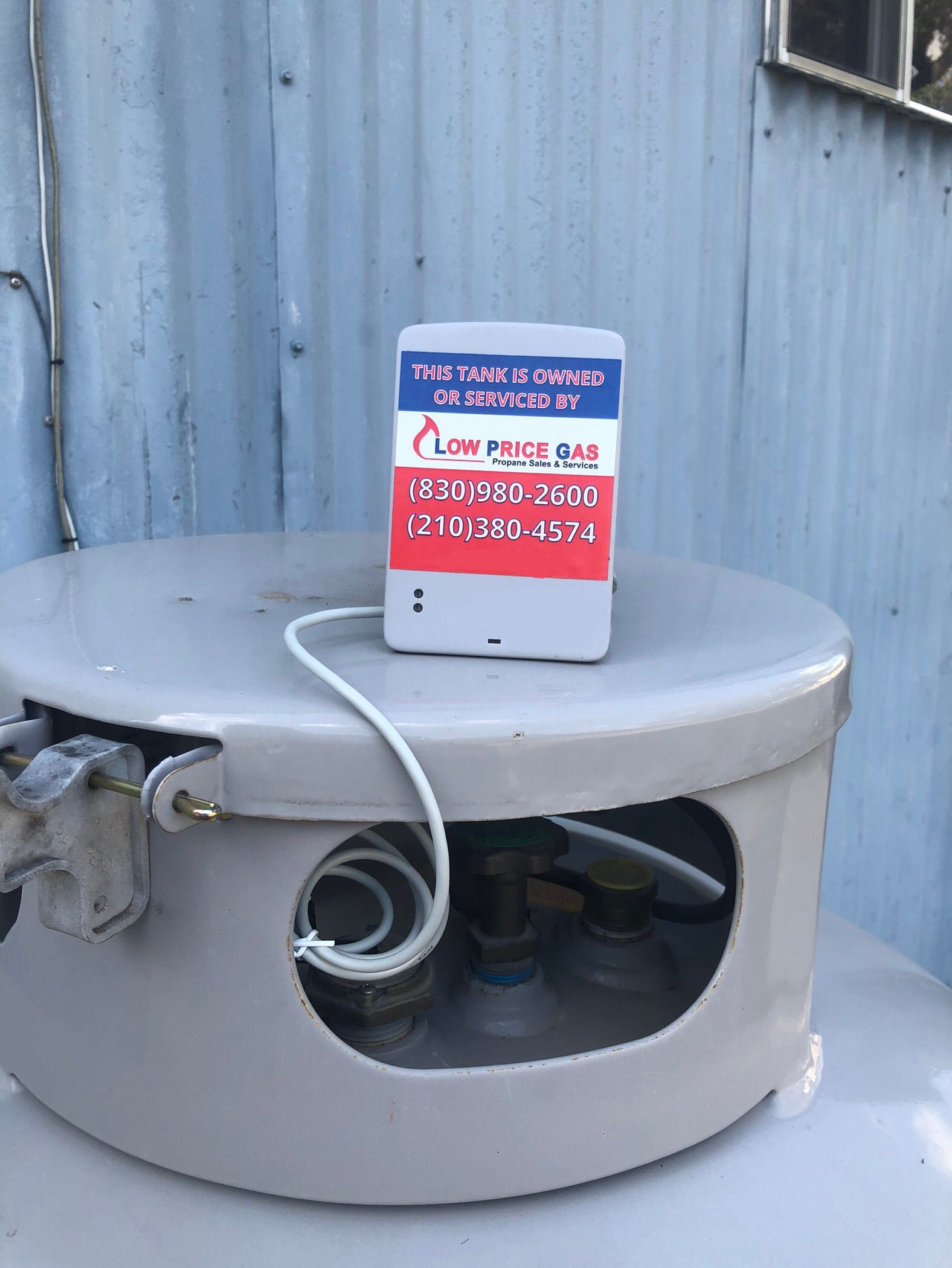 White cylindrical machine with a warning sign on top beside a corrugated metal wall.