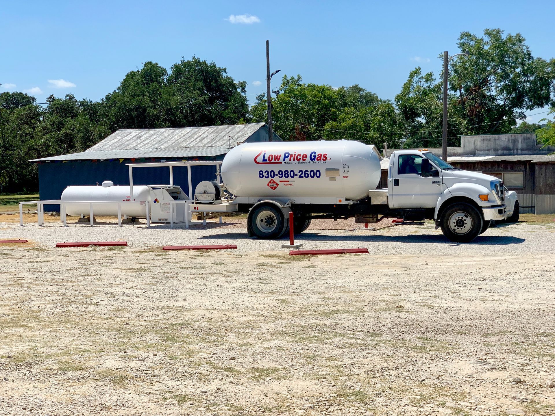 White tanker truck parked on a gravel lot under a sunny blue sky