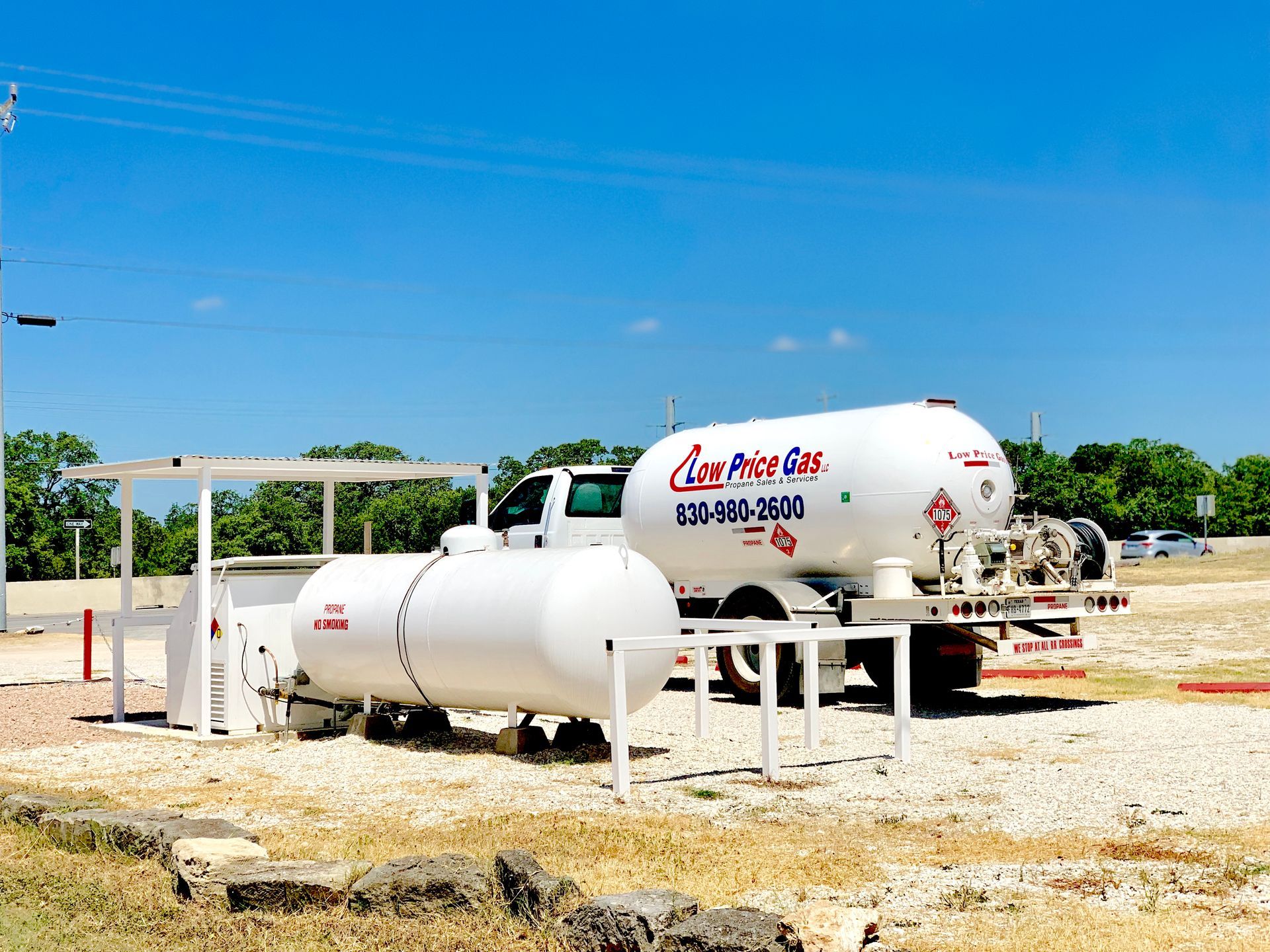 Two white propane tanks on a gravel lot under a clear blue sky