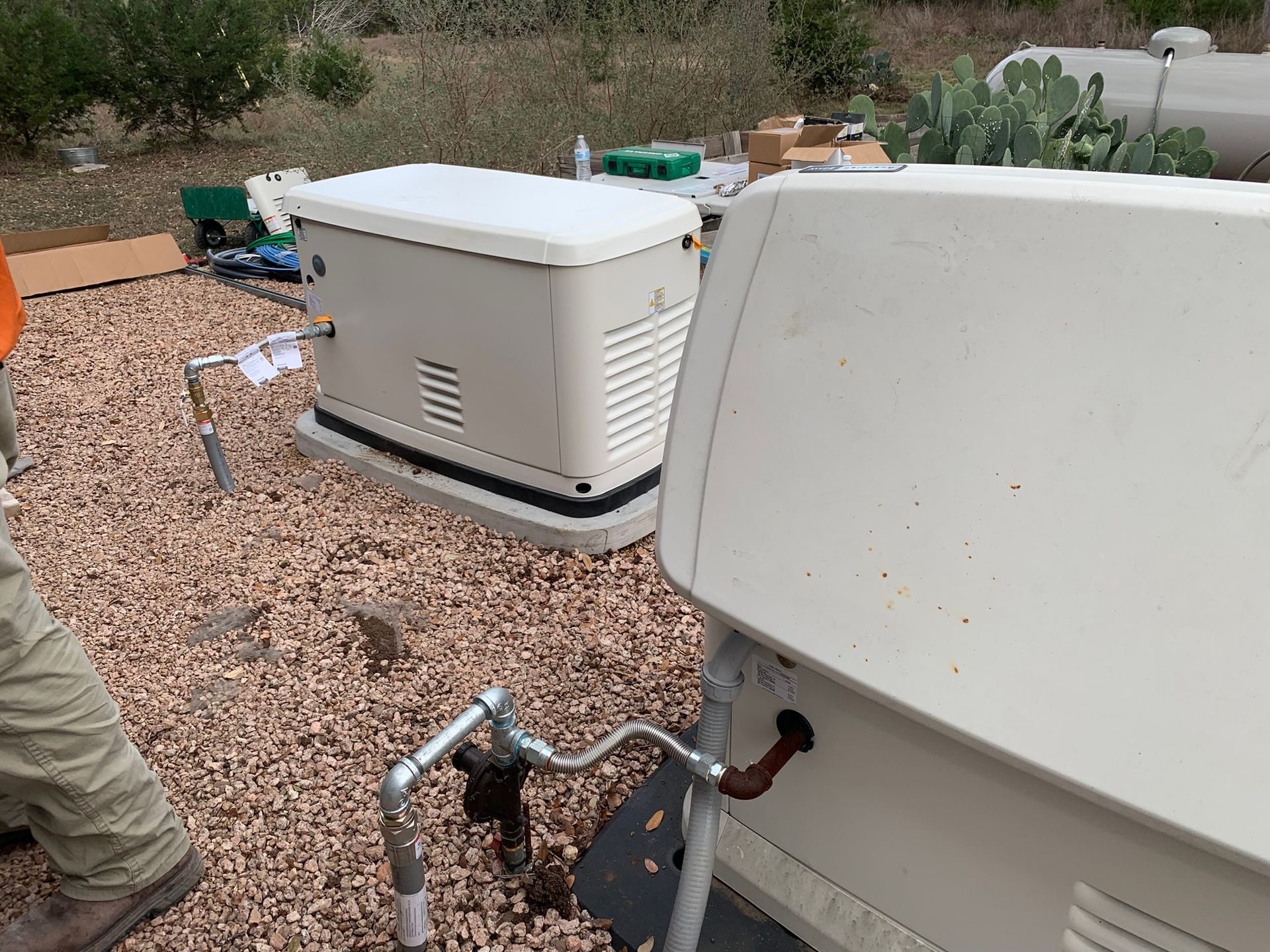 Two outdoor HVAC units connected by exposed copper and PVC pipes on gravel ground.
