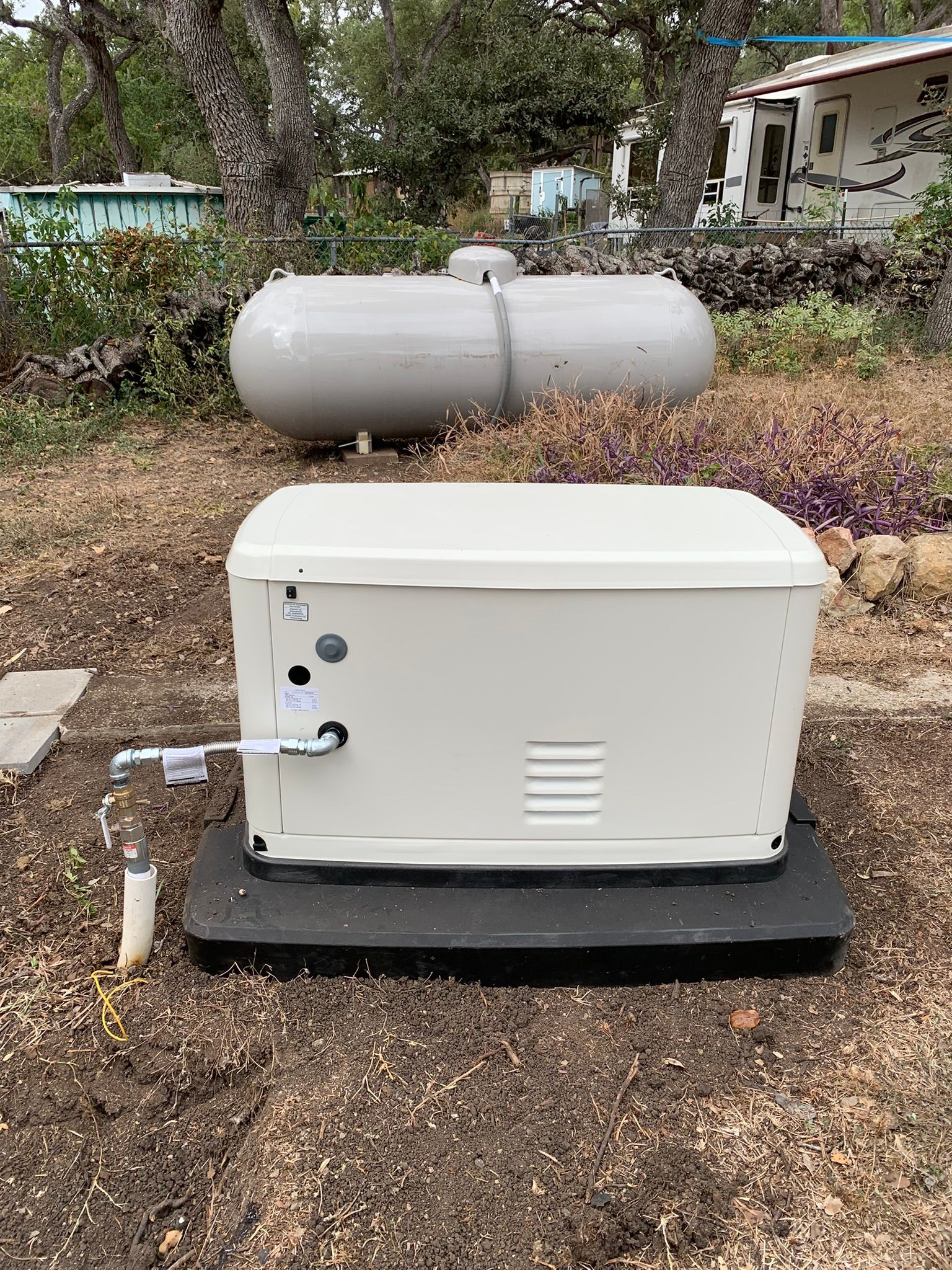 White generator on black pad beside a horizontal propane tank in a gravel yard