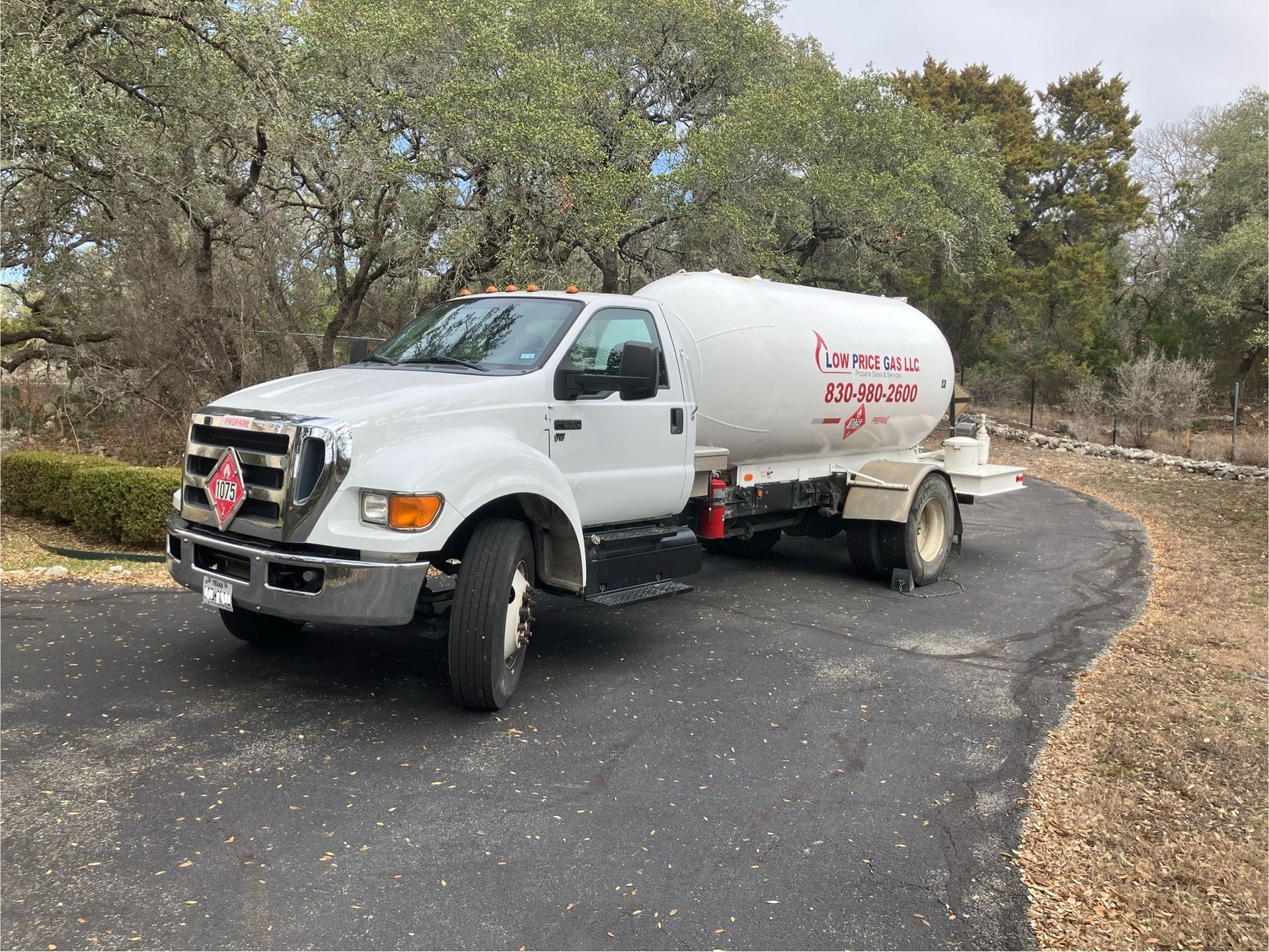 White water tanker truck driving on a curving gravel road amid trees and brush