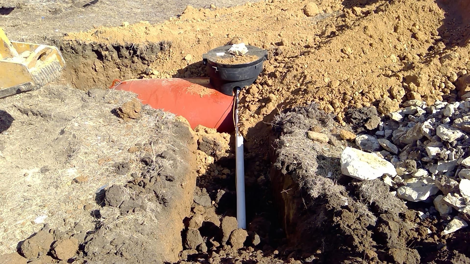 Survey marker post with a red flag in a dirt excavation site beside gravel.