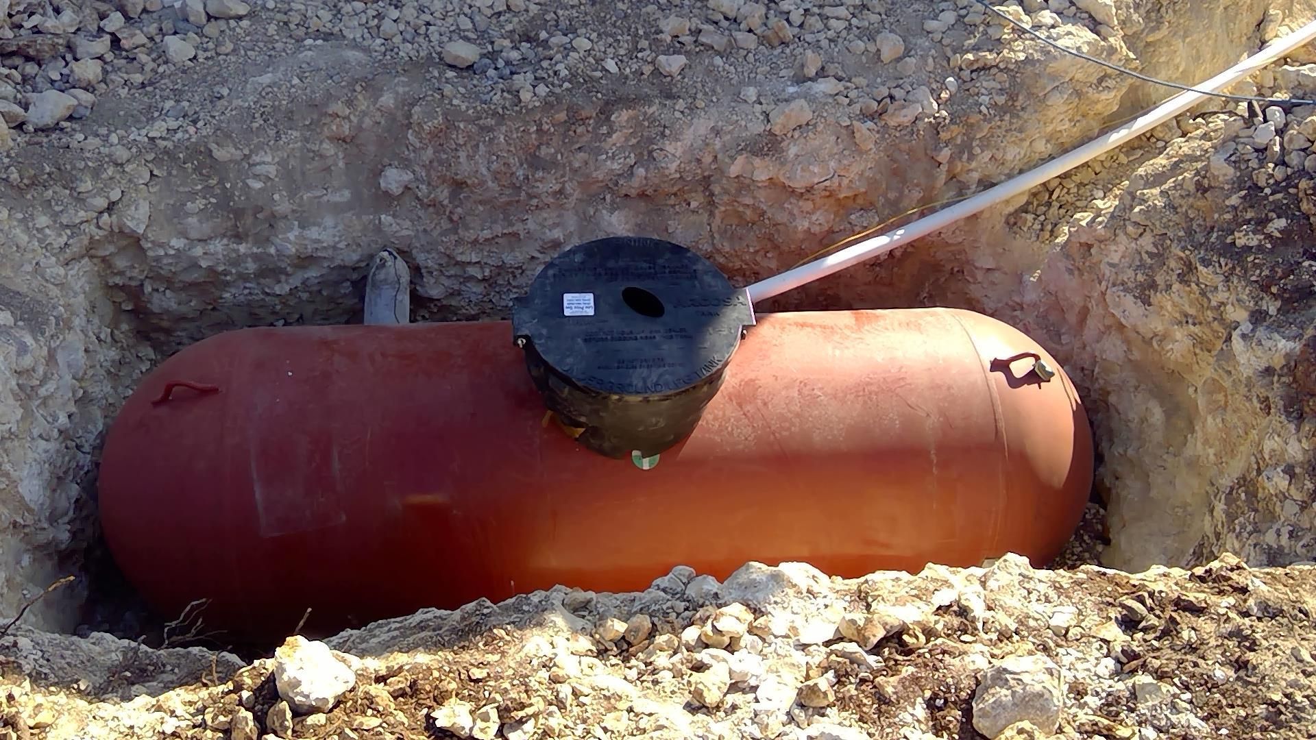 Buried orange cylindrical tank with a black cap in a dirt trench, outdoors