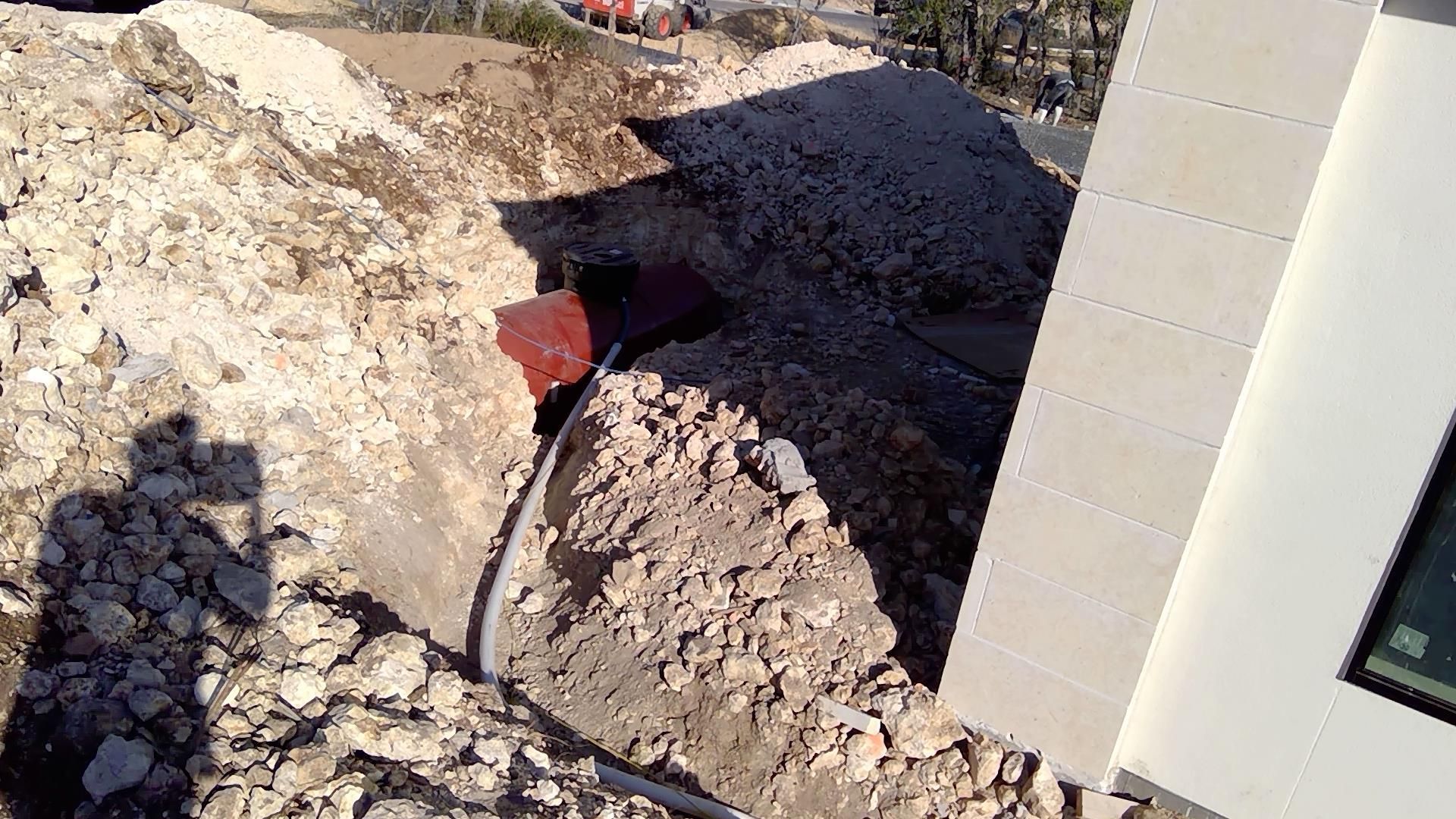 Construction site with large dirt pile beside a building and a red pipe in a trench