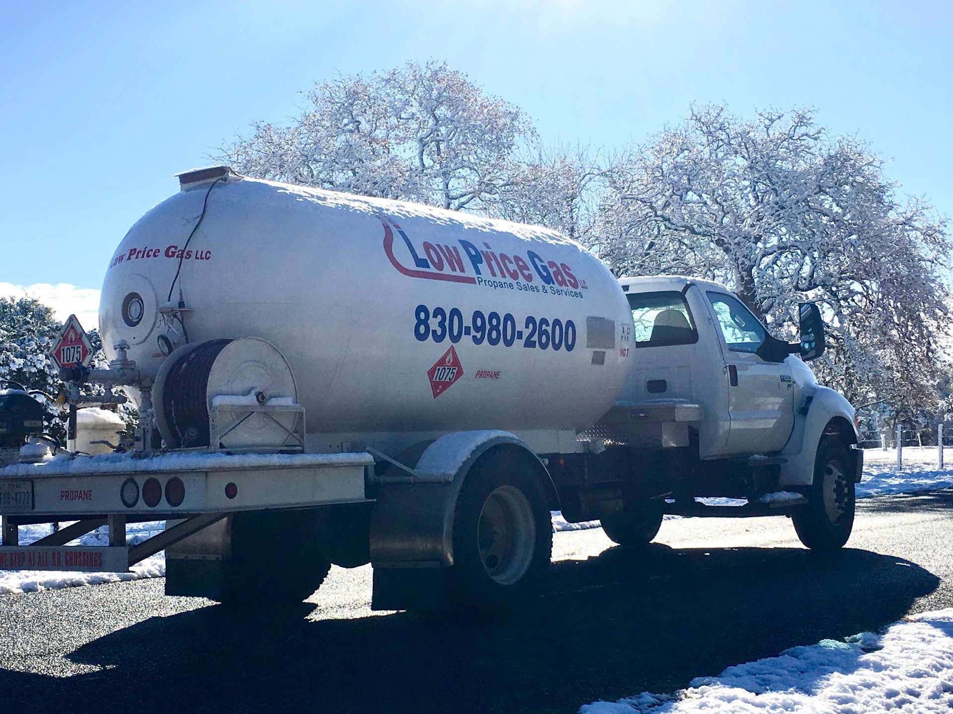 White vacuum tanker truck parked on a snowy roadside under bright sun