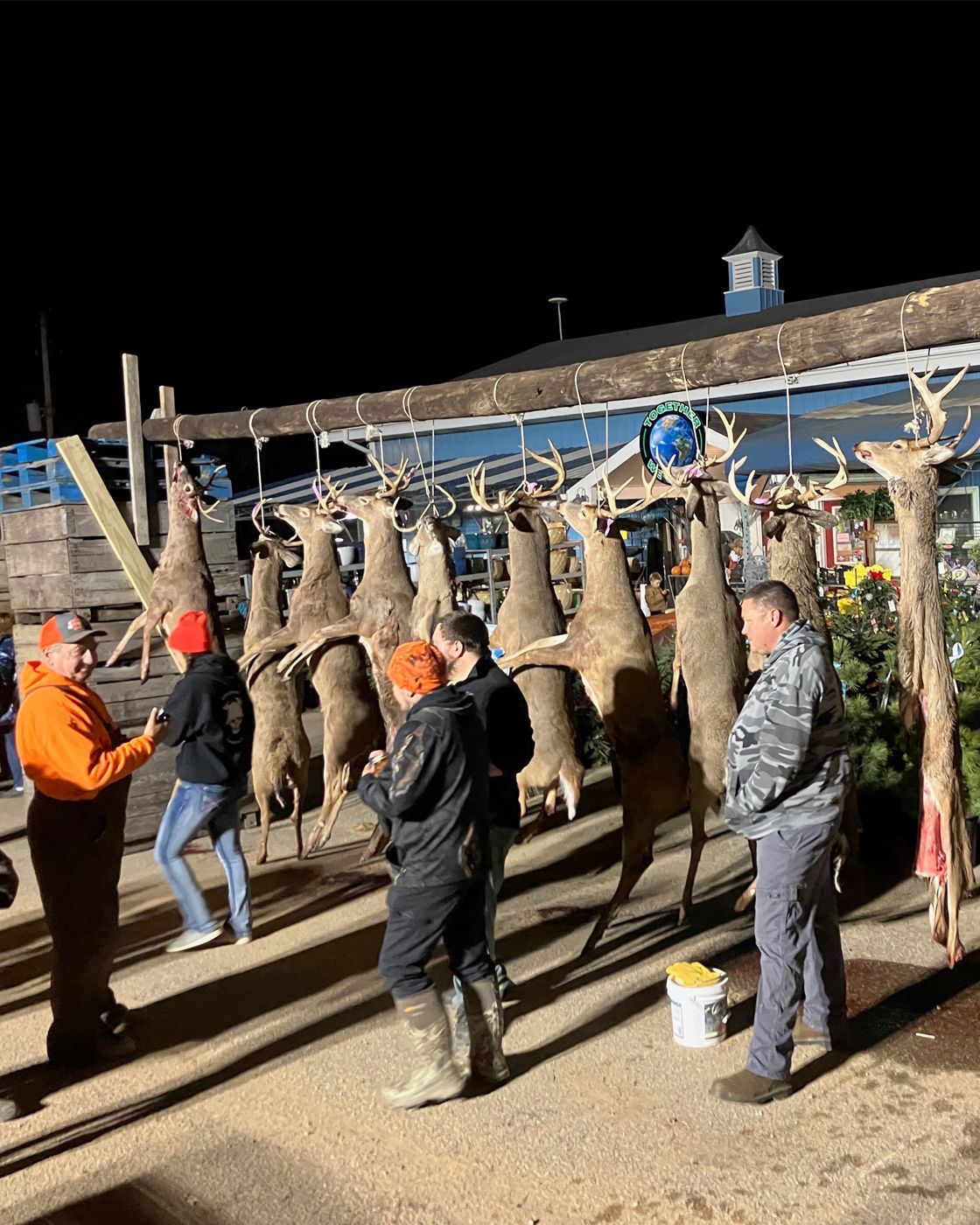 Men standing with deer hanging in the background.