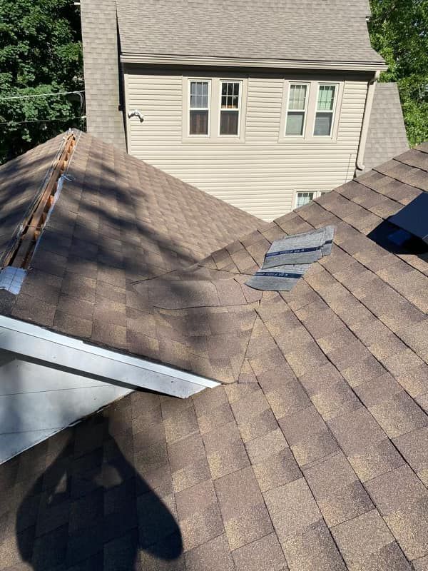 A roof with a hole in it and a house in the background.