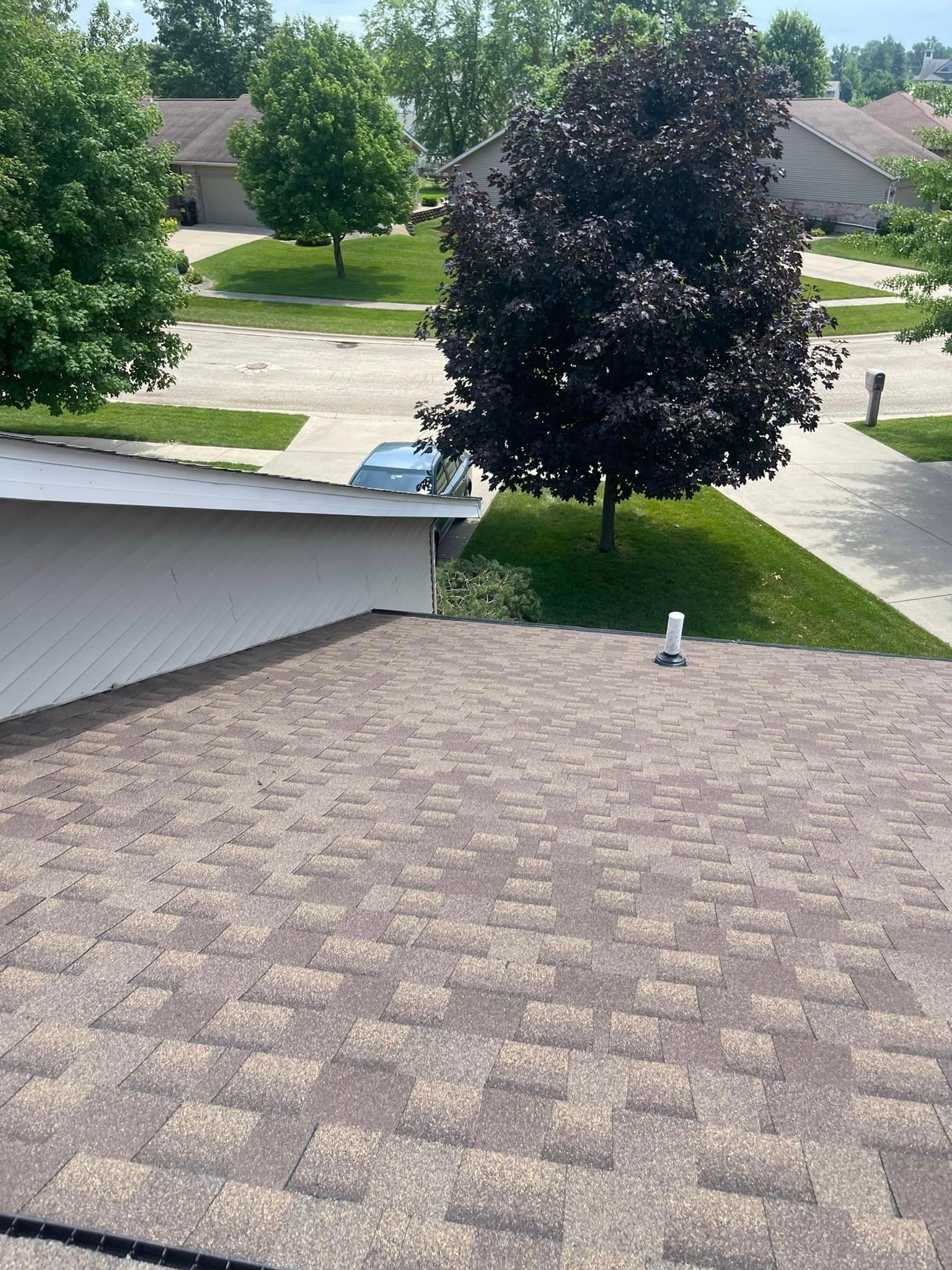The roof of a house with a purple tree in the background.