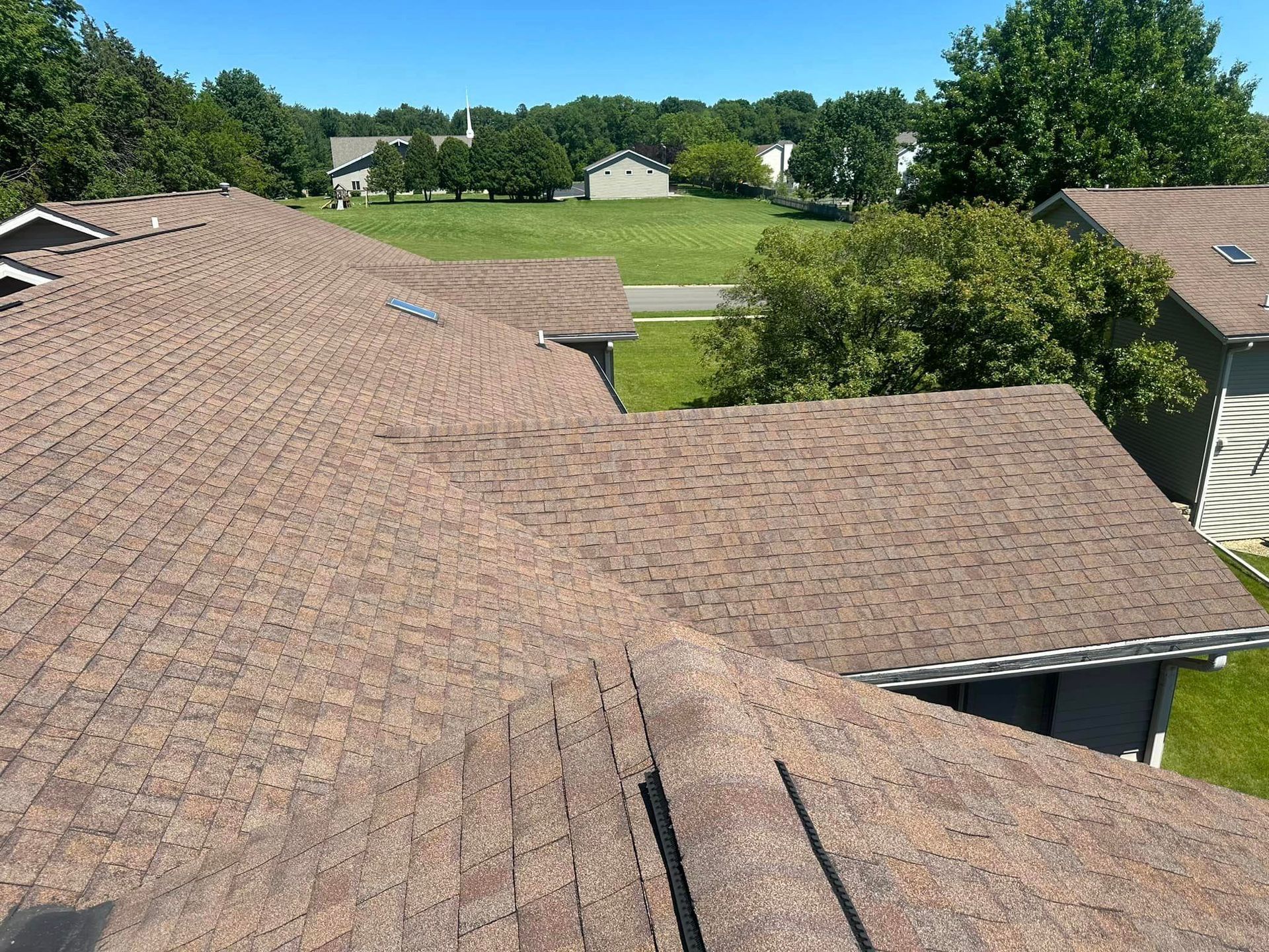 A roof of a house with a skylight and a field in the background.