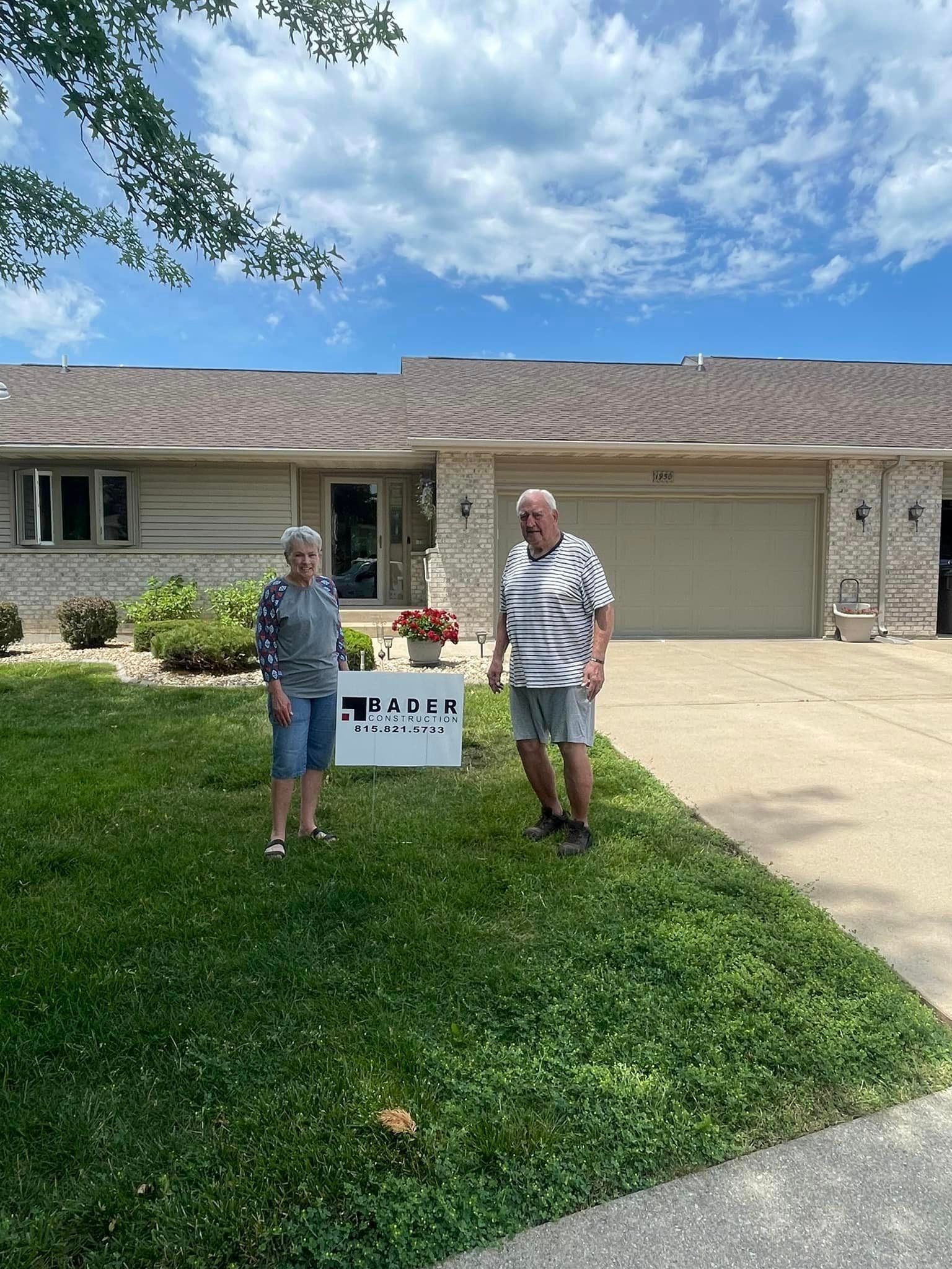 A man and a woman are standing in front of a house holding a sign.
