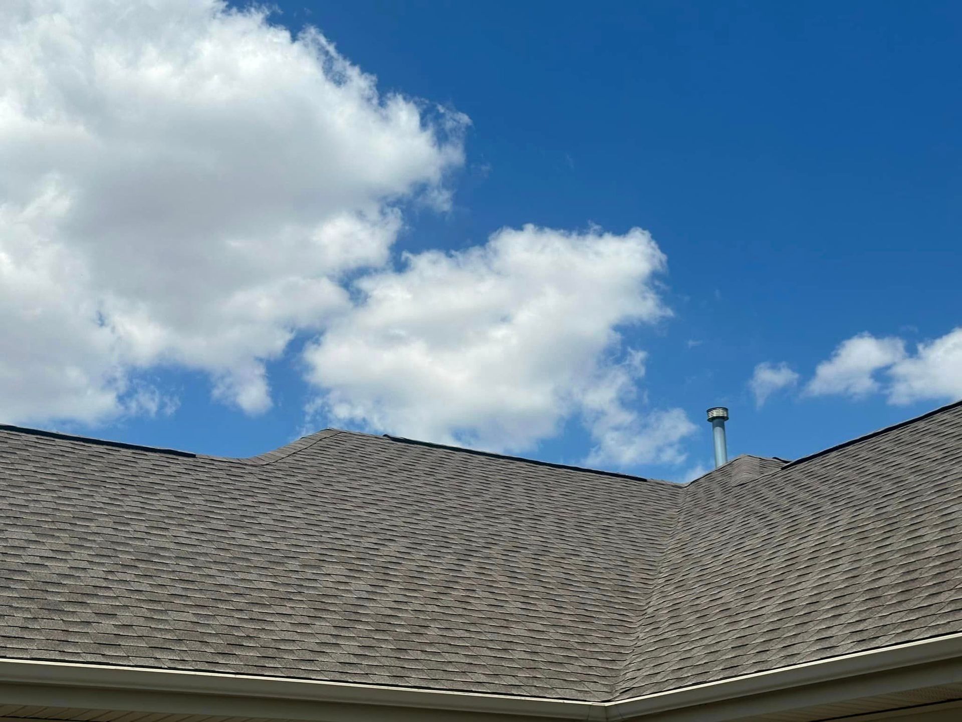 A roof with a chimney on top of it against a blue sky with clouds.