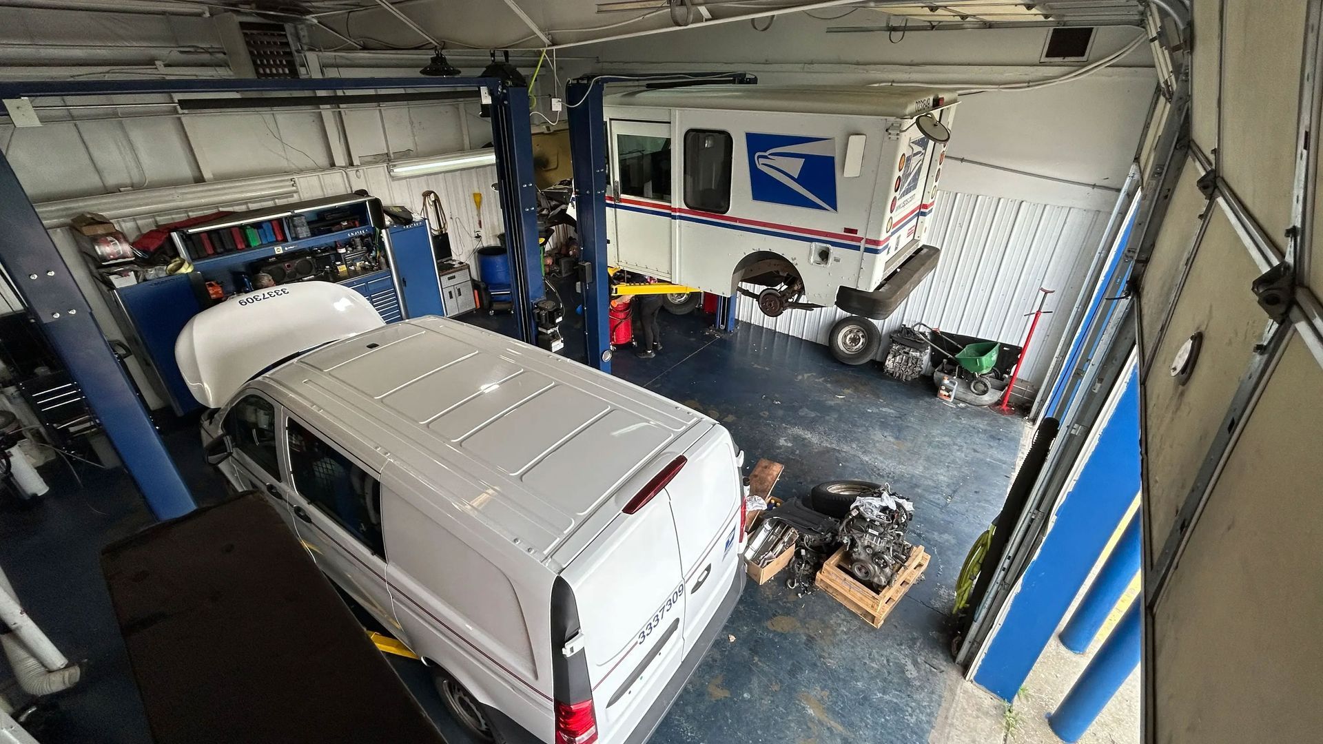 White van in a garage workshop with tools, bikes, and equipment around it