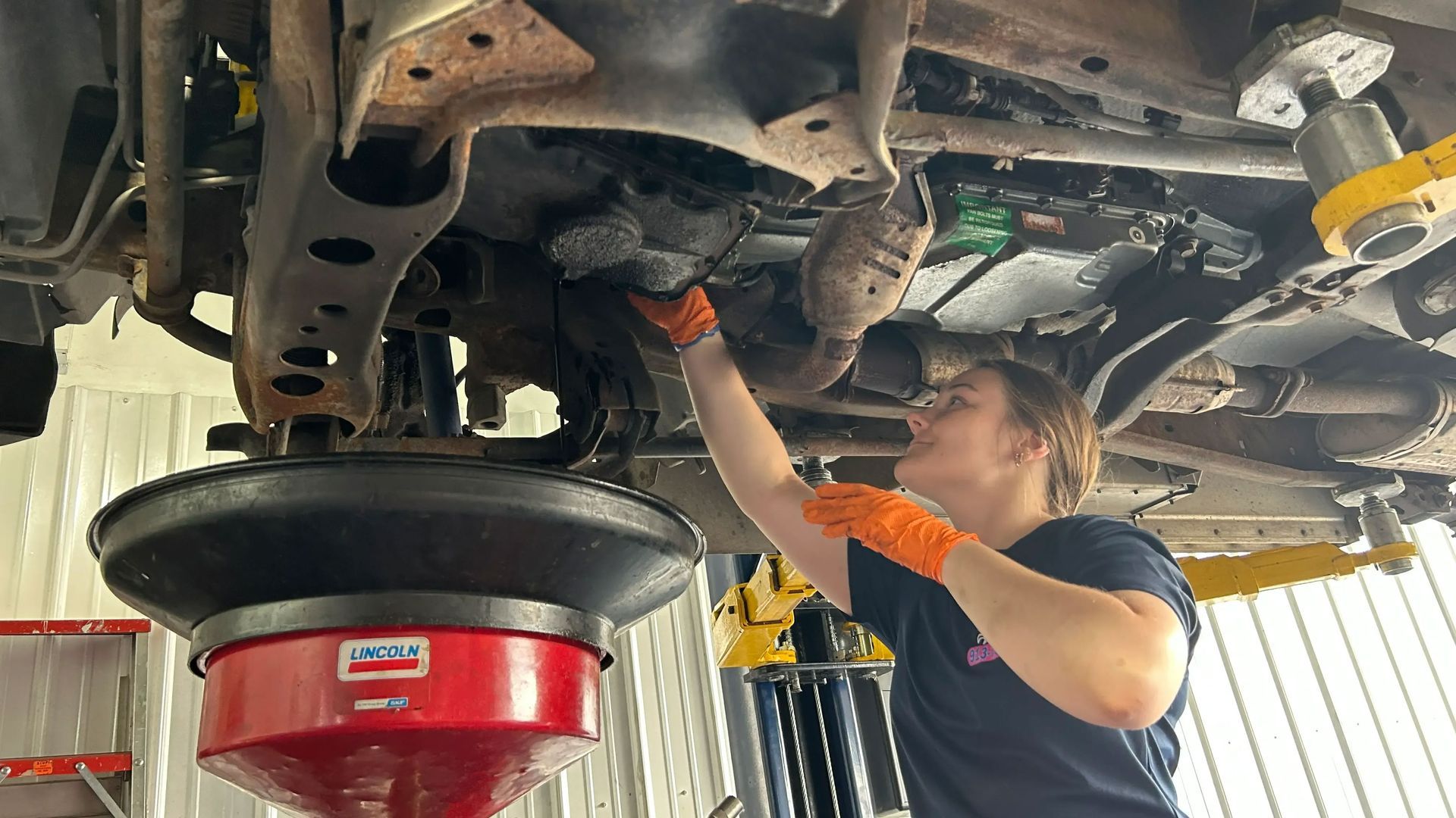 Mechanic working under a car on a lift, using tools in an auto repair shop