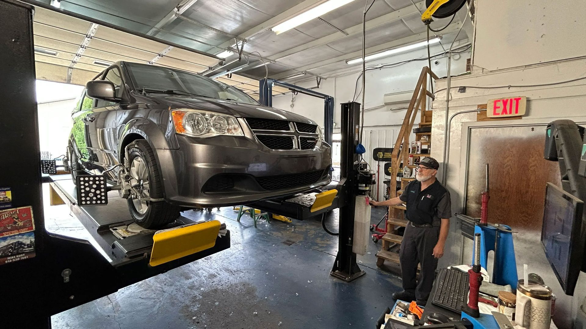 Dark gray SUV on a car lift in an auto repair shop, with a mechanic standing nearby.