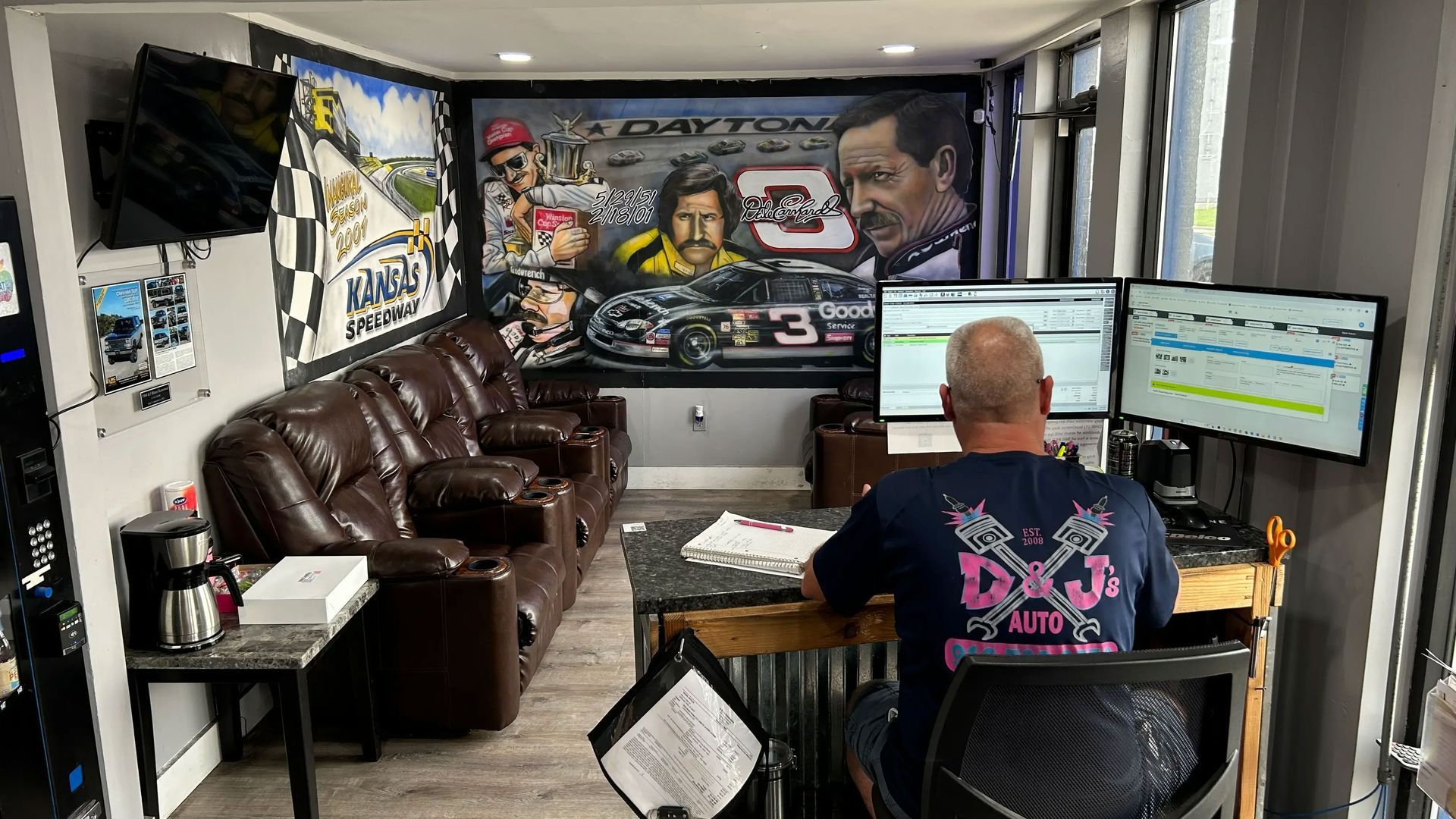 Home office with a person at dual monitors, brown couches, and graffiti-style wall art.