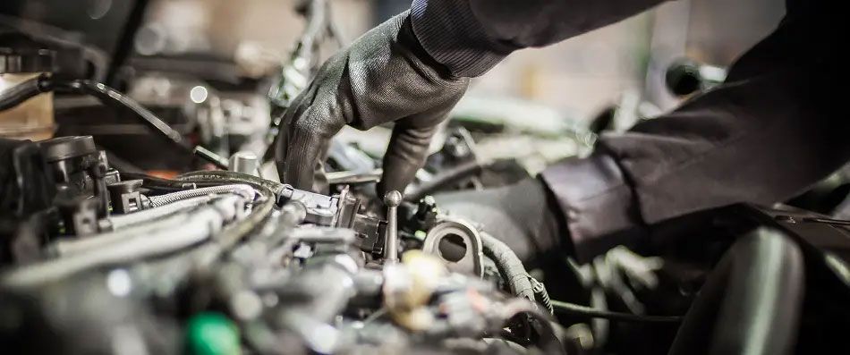 Mechanic working under a car engine, using tools in a dim garage