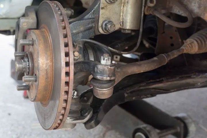 Close-up of a car’s front brake rotor, hub, and suspension components during repair.