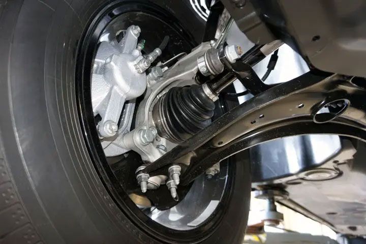Close-up of a car’s front wheel and suspension components underneath the vehicle.