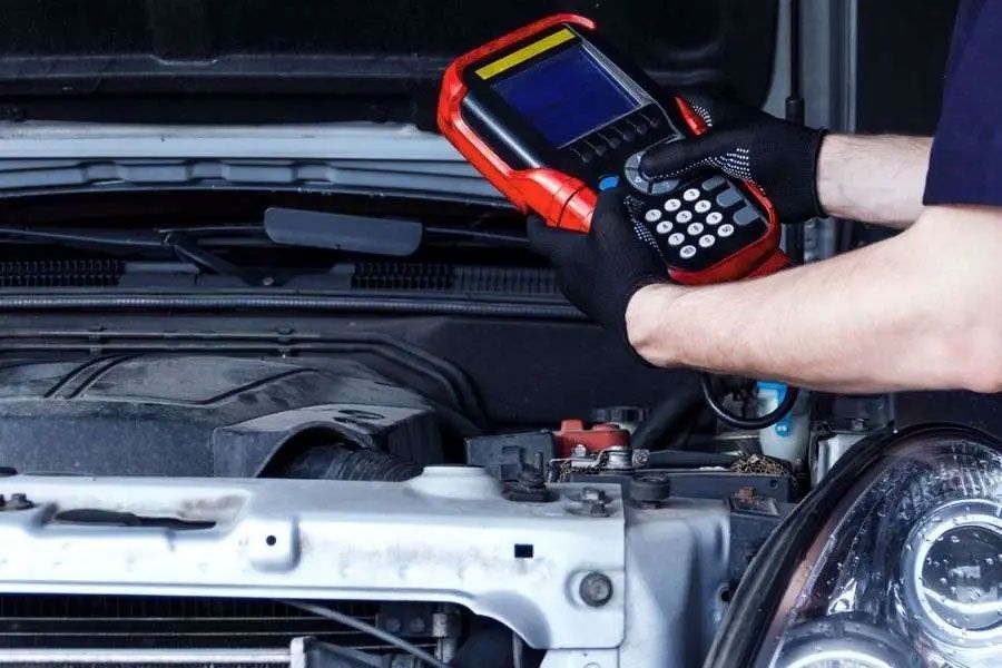 Person using a red diagnostic scanner on a car engine in an open hood compartment