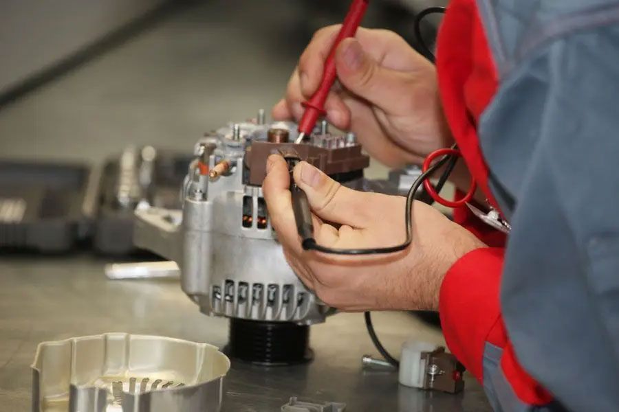 Technician testing a silver motor with red probes on a workbench