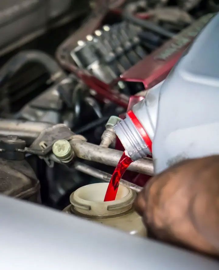 Red liquid being poured from a bottle into a car engine reservoir.
