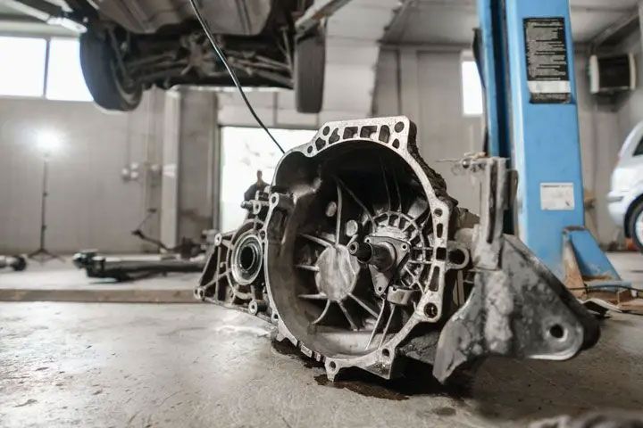 Damaged car transmission case on a garage floor near a hydraulic lift