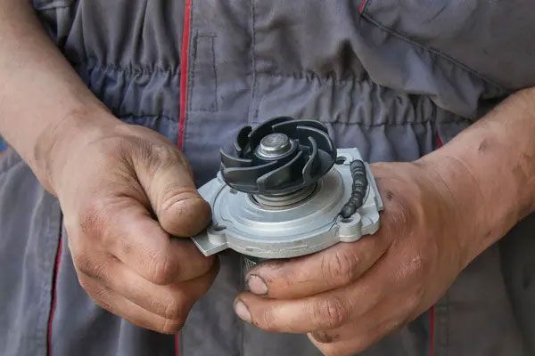 Hands holding a small metal mechanical part with a black plastic impeller.