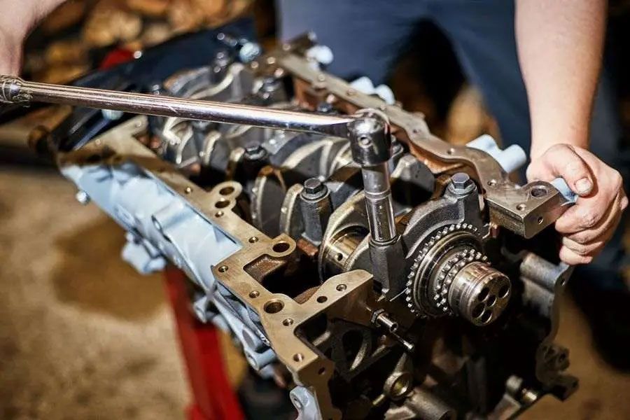Hands working on an exposed car engine with tools in a workshop