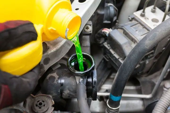 Green coolant being poured from a yellow container into a car engine reservoir.