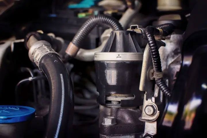 Close-up of an engine bay with black hoses, wiring, and a metallic fuel component.