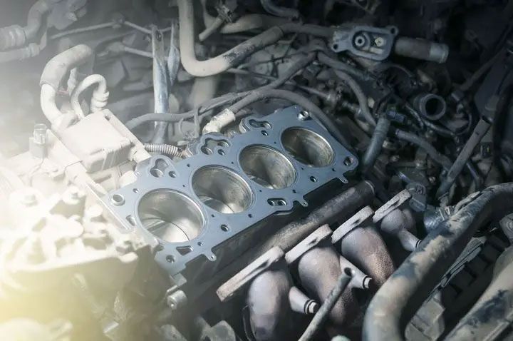 Engine cylinder head gasket on a cluttered workbench with hoses and metal parts.