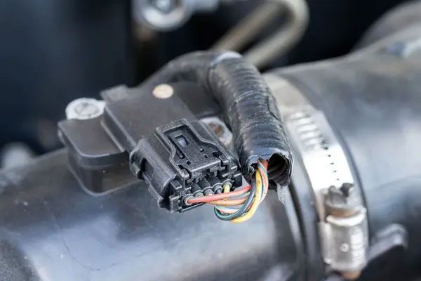 Close-up of a car mass air flow sensor mounted on an intake pipe with exposed colored wires