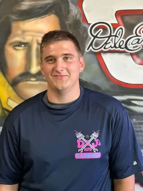 Person smiling in a navy shirt standing before a mural with a painted face and logo background