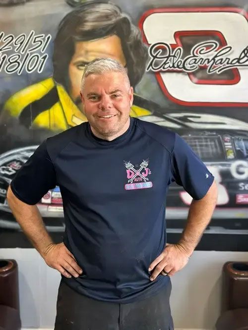 Smiling man in a navy shirt stands with hands on hips in front of a racing-themed mural.