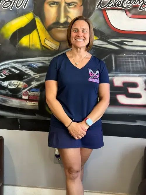 Smiling woman in navy shirt and shorts standing in front of a racing mural