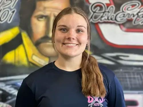 Smiling person in a dark shirt standing before a mural with a yellow-clad figure and stylized car graphic