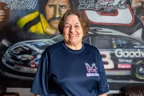 Smiling woman in navy shirt standing before a racing mural with a car and driver portrait
