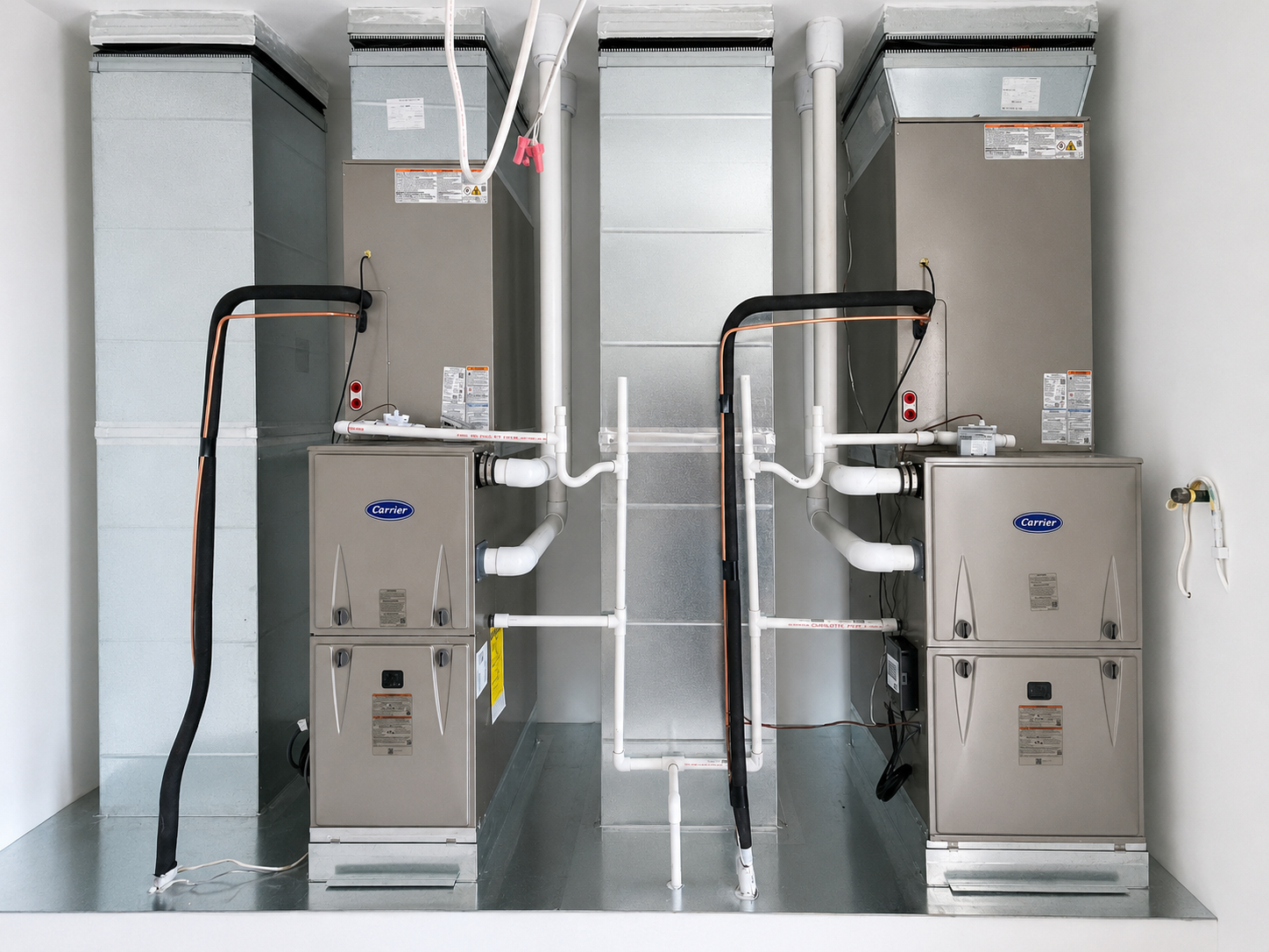 Two gray HVAC furnaces with white ducts and pipes in a utility room