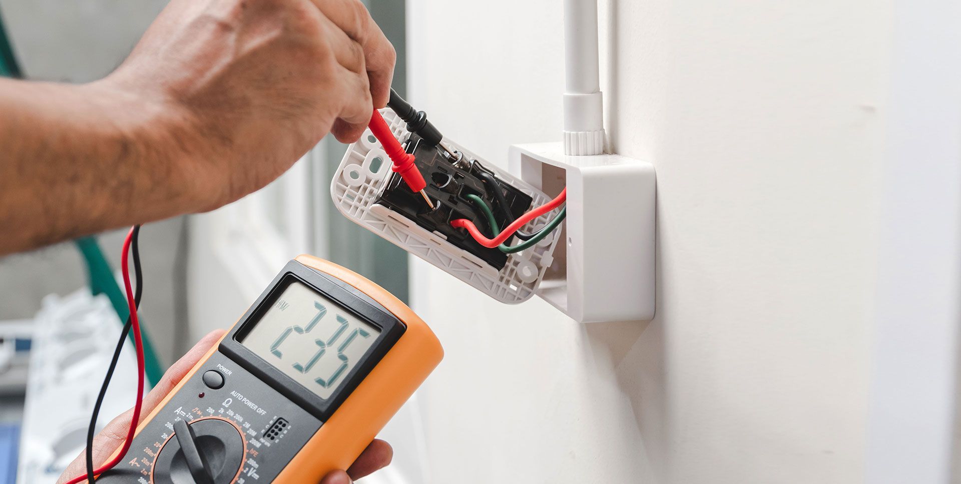 Electrician using a multimeter to test wires in an open wall electrical box