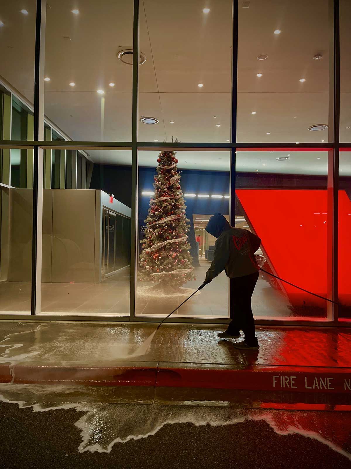 A man is cleaning the sidewalk in front of a building with a christmas tree in the background