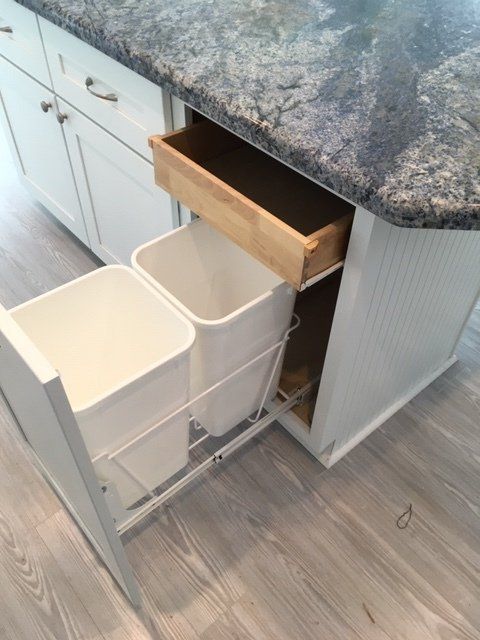 Two trash cans are pulled out of a drawer in a kitchen.
