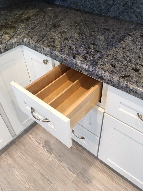 A kitchen with white cabinets and a wooden drawer