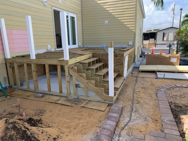 Wooden deck and stairs under construction beside a beige house, with unfinished framing and sandy yard.