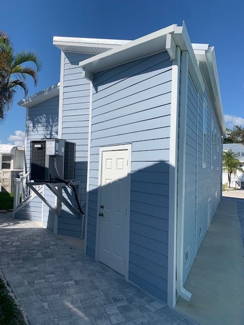 Light blue house with white trim, door, and guttering, AC unit. Brick walkway.