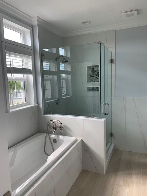 Bathroom with a white bathtub, glass shower, and marble tile accents. Window on the left side.